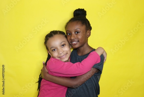 Two little brown skin girls hugging studio yellow background