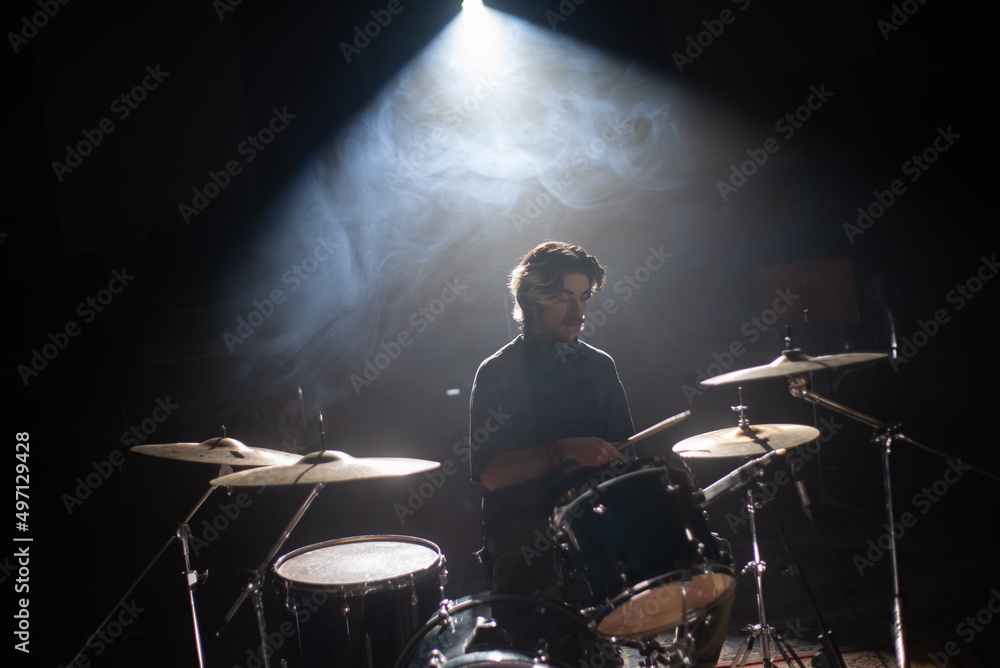 Concentrated young drummer training in dark hall with smoke in background. Rock musician rehearsing on drum set in studio. Drummer training concept Concentrated young drummer training in dark hall with smoke in background. Rock musician rehearsing on drum set in studio. Drummer training concept
