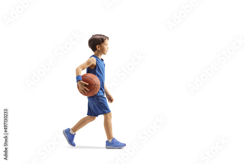 Full length profile shot of a boy in a blue jersey walking and holding a basketball