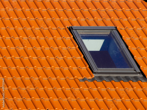 Window on roof of house with orange roof tiles on a background of blue sky