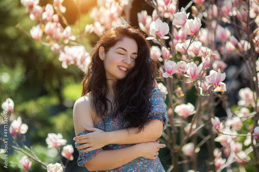 Fototapeta premium Beautiful girl with flowers of magnolia. Portrait of young smiling brunette woman under blossom magnolia tree.