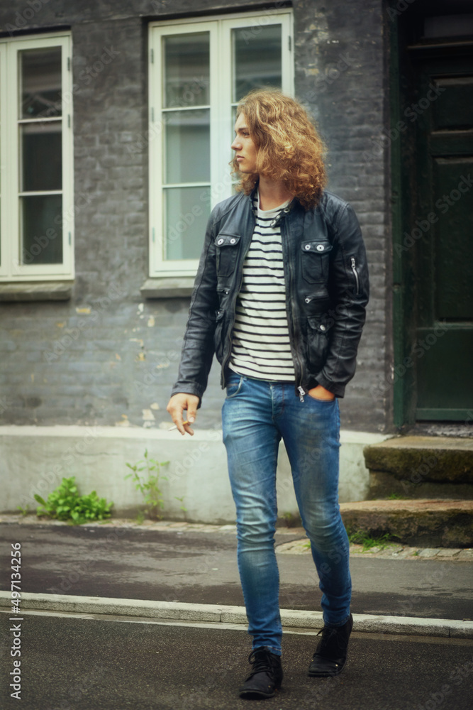 Breaking all the rules. A handsome young man walking across a road with a cigarette in his hand. Breaking all the rules. A handsome young man walking across a road with a cigarette in his hand.