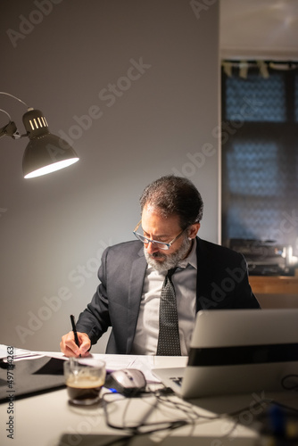 Focused bearded man working late at night. Man in suit sitting at table with laptop  thinking. Business  job  occupation  late night work concept