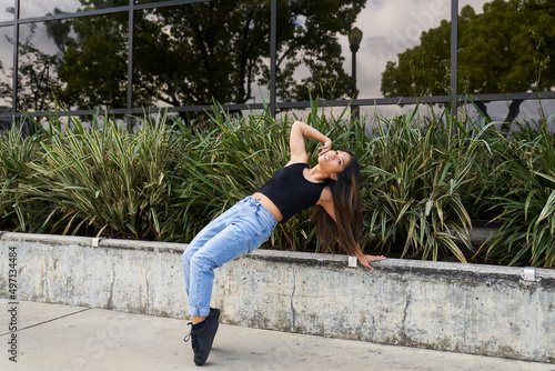 Woman dancing leaning back on concrete wall with plants