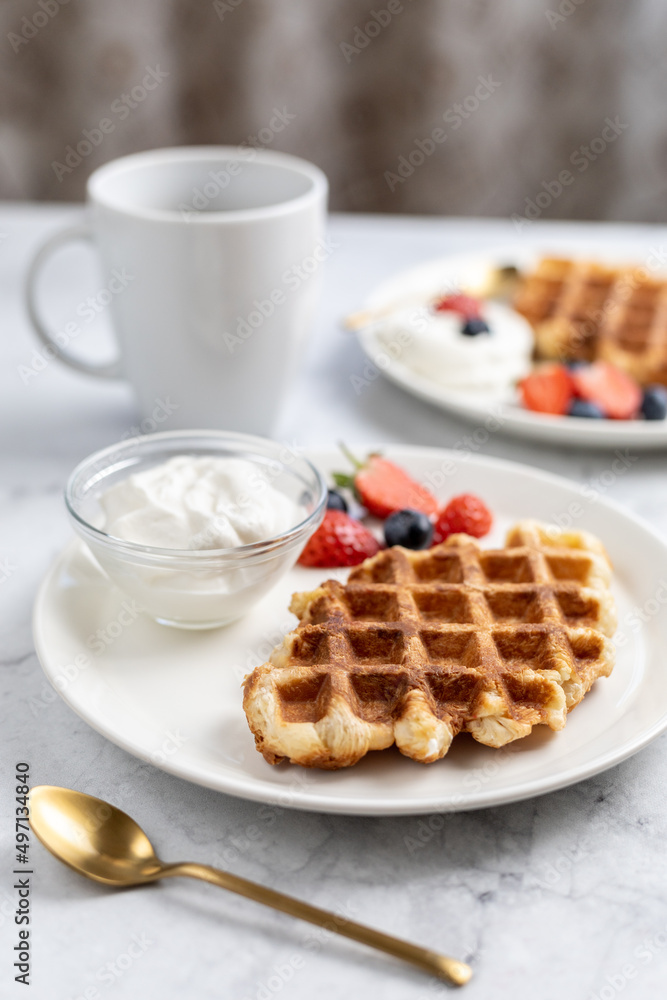 Vertical photo of sweet breakfast. Croffles (croissant waffle) with whipped cream and berries, cup of coffee. Vertical photo of sweet breakfast. Croffles (croissant waffle) with whipped cream and berries, cup of coffee.
