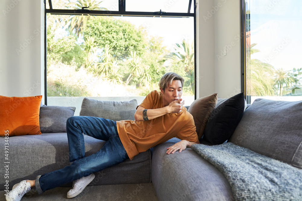 Man with hands touching face on sofa by window Man with hands touching face on sofa by window