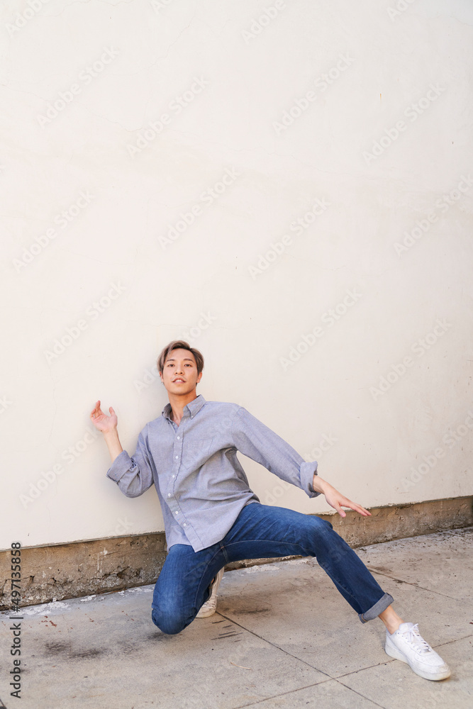 Man dancing by wall on concrete sidewalk with knee bent Man dancing by wall on concrete sidewalk with knee bent