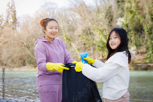 Earth Day concept, Woman and daughter pick up garbage in litter bags, clean-ups in nature to recycling in their communities, clean river and protect environment from pollution, conservation Nature.