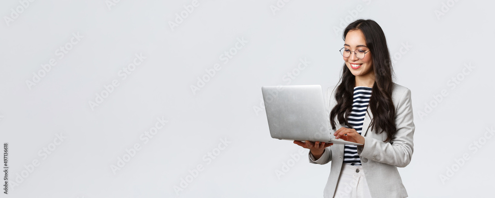 Business, finance and employment, female successful entrepreneurs concept. Professional stylish asian businesswoman fixing project on her way to office, using laptop standing whtie background - obrazy, fototapety, plakaty 