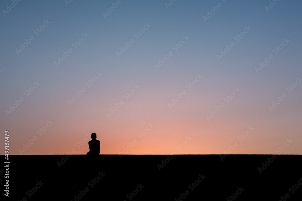 Junge sitzt auf Mauer nach Sonnenuntergang