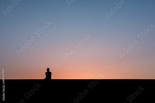 Junge sitzt auf Mauer nach Sonnenuntergang