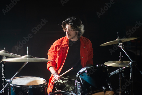 Serious young Caucasian drummer rehearsing in studio. Man playing drums set or recording music. Drummer training concept