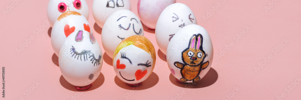 The banner is made of Easter eggs drawn by children with felt-tip pens with different painted faces on a pink background. Emotions of joy, love and shyness. Pink bunny. Minimal concept, Copy space.