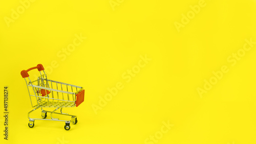Shopping trolley, cart empty on yellow spot. The concept of Promotions, sales, shopping, advertising, ad, mocap, place for text High quality photo