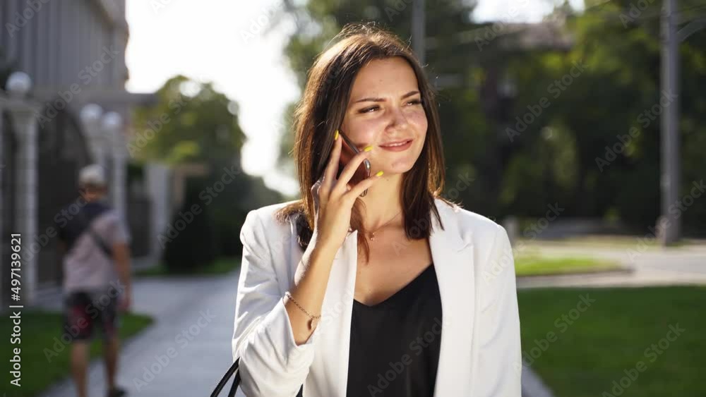 A young smart girl is walking and talking on a smartphone. A tanned pretty girl in a white suit walks down the street. Successful businesswomen on lunch break. A young smart girl is walking and talking on a smartphone. A tanned pretty girl in a white suit walks down the street. Successful businesswomen on lunch break.