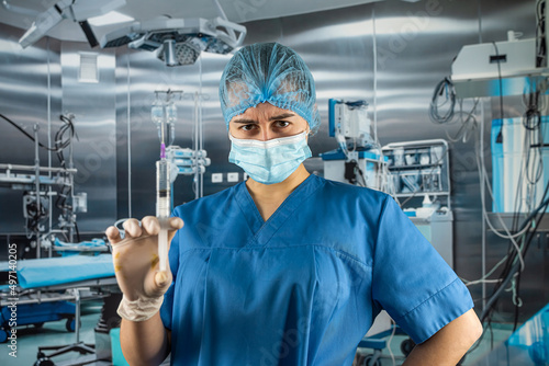 nurse in blue uniform with gloves mask holding a syringe with medication and waiting for patient