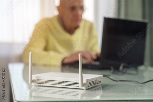 Foto Wifi router with antenna stands on table against blurred man sitting on chair an