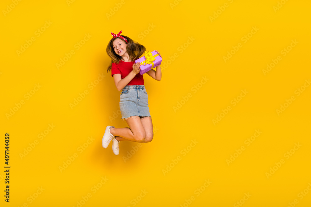 Full body photo of cute teenager girl jump hold present wear t-shirt hairband skirt footwear isolated on yellow background Full body photo of cute teenager girl jump hold present wear t-shirt hairband skirt footwear isolated on yellow background