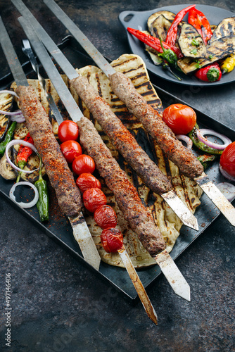 Traditional Turk Adana kebap on shashlik skewer with barbecue vegetable and flatbread served as close-up on a rustic metal tray