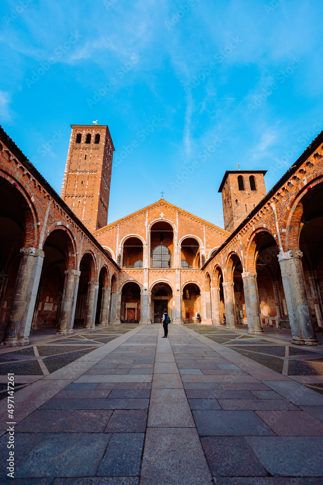 Wide view of the Basilica of Sant'Ambrogio with a tourist in the center of the courtyard, vertical