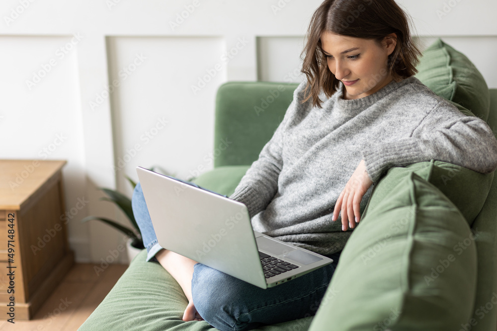 Young beautiful smiling woman using laptop lying on the couch. Concept of freelance job, home office. Female using technology for learning, shopping, e-commerce, communication, social media Young beautiful smiling woman using laptop lying on the couch. Concept of freelance job, home office. Female using technology for learning, shopping, e-commerce, communication, social media