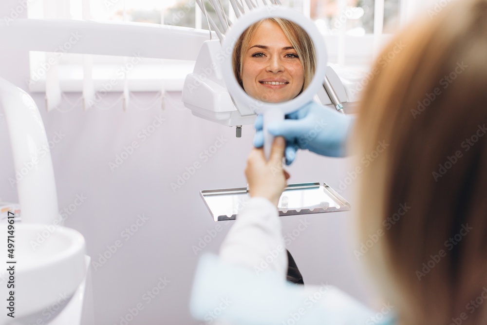 A woman looks and smiles in the mirror after a visit to the dentist A woman looks and smiles in the mirror after a visit to the dentist