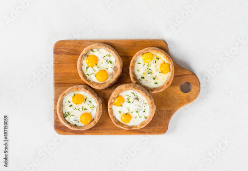 Mini open rye cottage cheese pies with mozzarella, quail eggs and dill, on a wooden board. White background. Top view