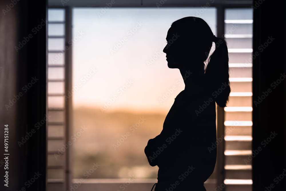 Woman in a dark room looking out window early morning 