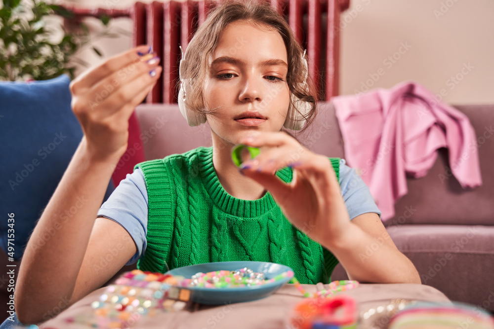 Female teenager looking at her new hand made ring and listening music in big headphones Female teenager looking at her new hand made ring and listening music in big headphones