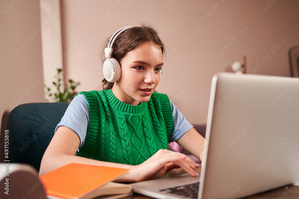 Teen wearing headphones typing at the laptop computer while doing her homework Teen wearing headphones typing at the laptop computer while doing her homework