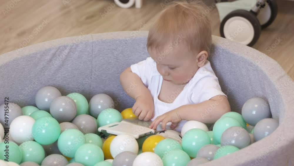 Kid playing with smartphone in ball pit at home. Happy kid lying in soft ball pit pool with colorful balls for toddlers, caucasian baby boy having fun playing at home. . High quality 4k footage Kid playing with smartphone in ball pit at home. Happy kid lying in soft ball pit pool with colorful balls for toddlers, caucasian baby boy having fun playing at home. . High quality 4k footage