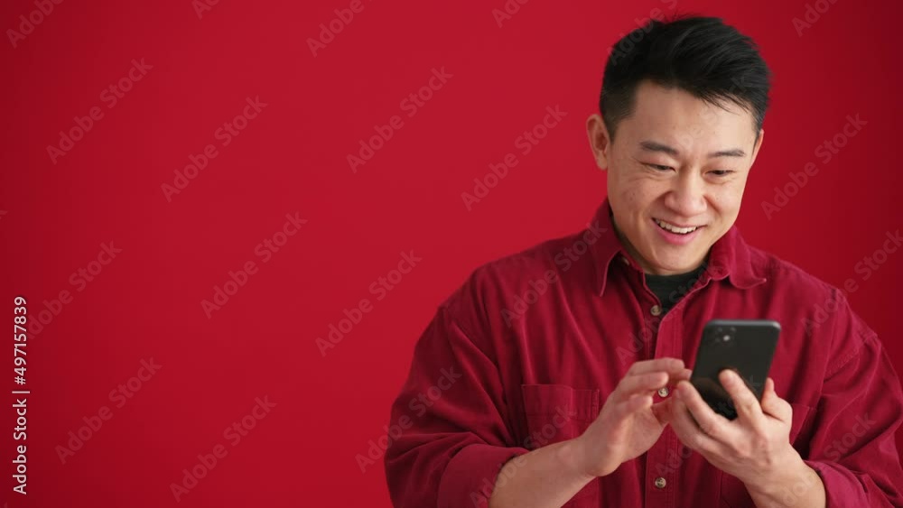 Surprised Asian man wearing shirt looking at phone and showing different gestures in the red studio Surprised Asian man wearing shirt looking at phone and showing different gestures in the red studio