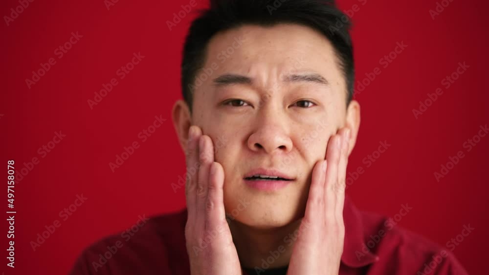 Cheerful Asian man wearing shirt correcting his appearance at the camera in the red studio Cheerful Asian man wearing shirt correcting his appearance at the camera in the red studio