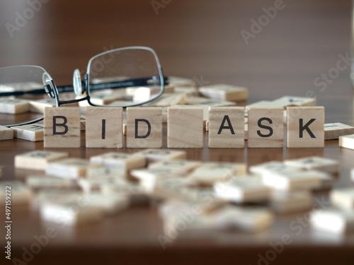 bid ask word or concept represented by wooden letter tiles on a wooden table with glasses and a book photo