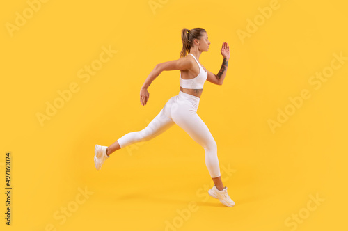 energetic sport woman runner running on yellow background © Olena