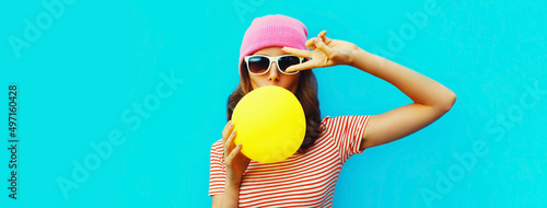 Fashionable portrait of stylish cool young woman inflating chewing gum wearing pink hat on blue background