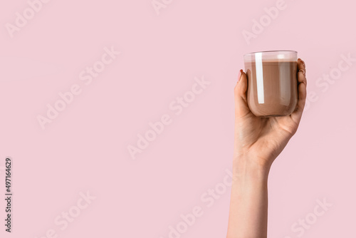 Female hand holding glass of delicious chocolate milk on color background