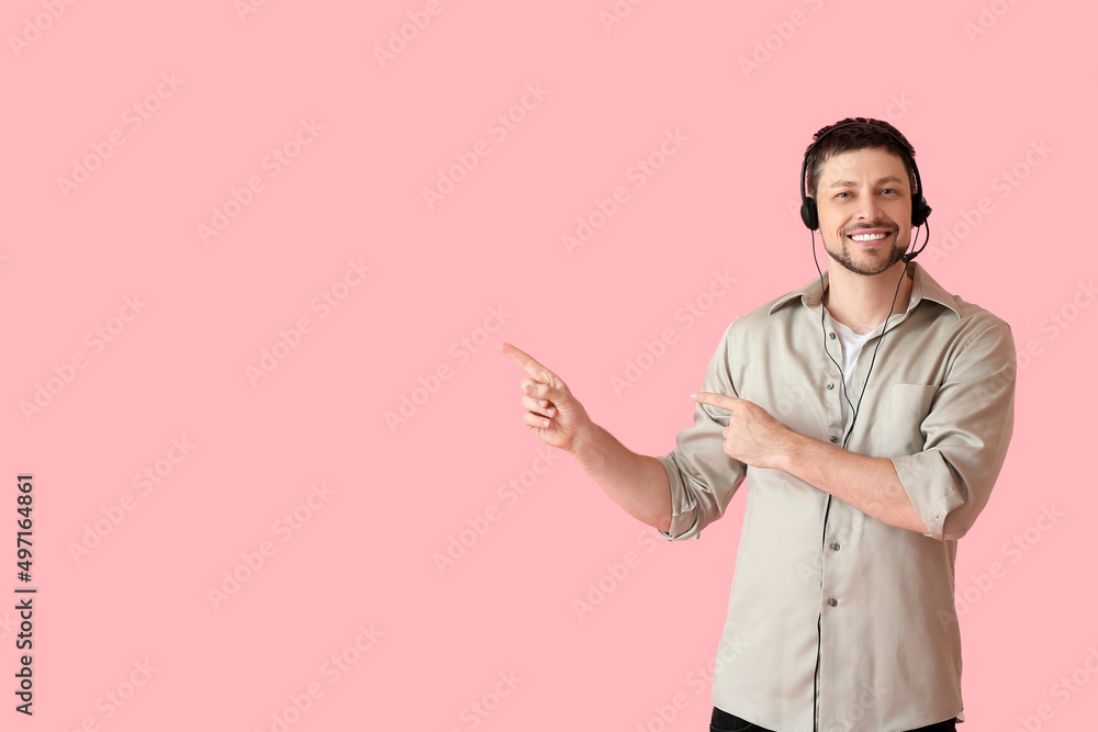 Smiling consultant of call center in headset pointing at something on pink background Smiling consultant of call center in headset pointing at something on pink background