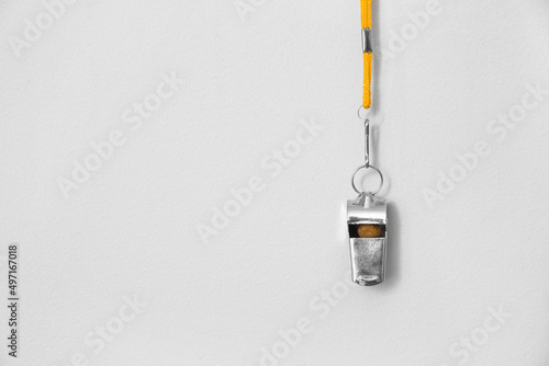 Lifeguard's whistle hanging on light wall, closeup photo