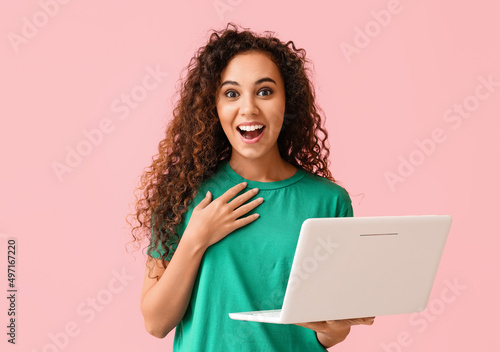 Surprised young African-American woman with laptop on pink background © Pixel-Shot