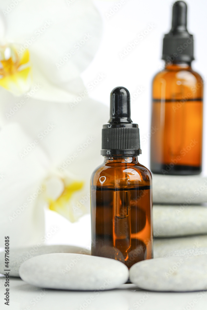 Beauty and aromatherapy.Massage oil and massage stones.glass bottle with oil on gray stones and white orchid flower on white background.Spa and relaxation. orchid flower, massage stones and oil Beauty and aromatherapy.Massage oil and massage stones.glass bottle with oil on gray stones and white orchid flower on white background.Spa and relaxation. orchid flower, massage stones and oil