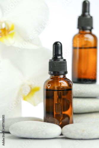 Beauty and aromatherapy.Massage oil and massage stones.glass bottle with oil on gray stones and white orchid flower on white background.Spa and relaxation. orchid flower, massage stones and oil 