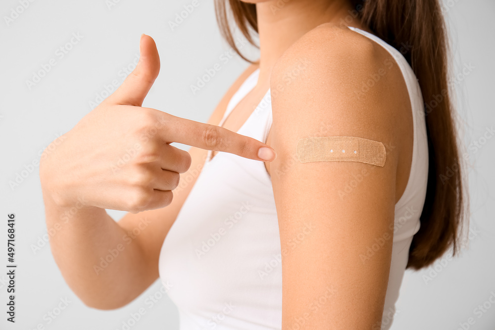 Young woman pointing at applied medical patch on light background, closeup
