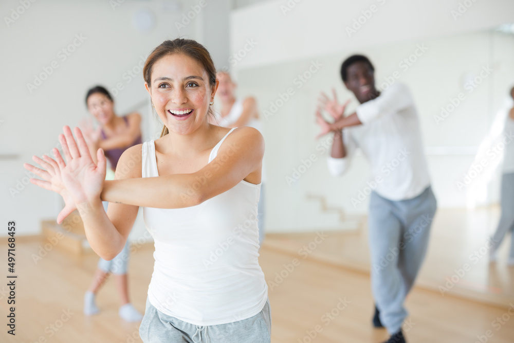 Cheerful young hispanic woman practicing vigorous lindy hop movements during group training in dance studio.