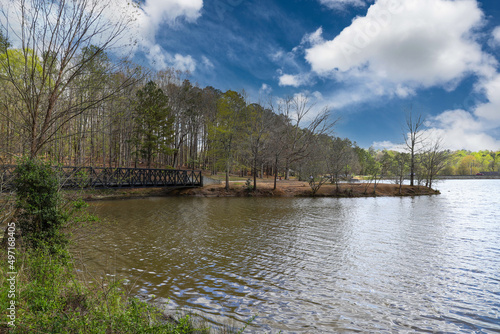 a black metal bridge over a rippling lake surrounded by bare winter trees and lush green trees with powerful clouds and blue sky at Murphey Candler Park in Atlanta Georgia USA photo