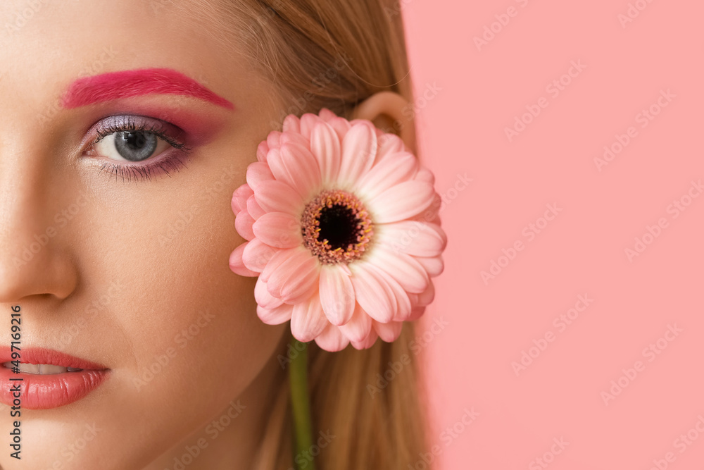 Young woman with creative makeup and gerbera flower on color background, closeup