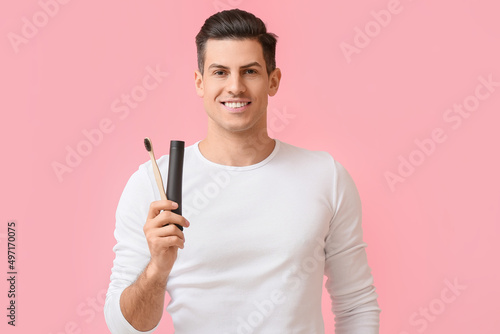 Handsome young man with activated charcoal tooth paste and brush on pink background