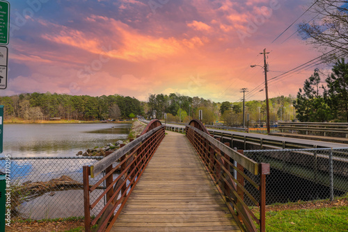 a metal and wooden rust colored bridge over a lake surrounded by lake water, green grass and lush green trees with powerful clouds and red sky at sunset at Murphey Candler Park in Atlanta Georgia USA photo