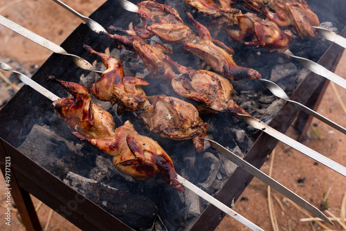 Cooking marinated quails on skewers, on the grill