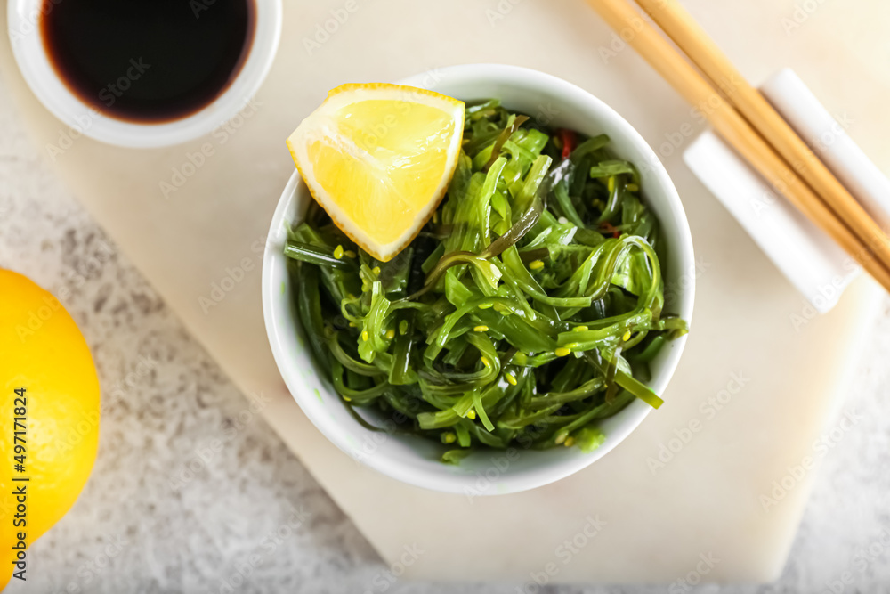 Bowl with healthy seaweed salad, lemon and sauce on light background Bowl with healthy seaweed salad, lemon and sauce on light background